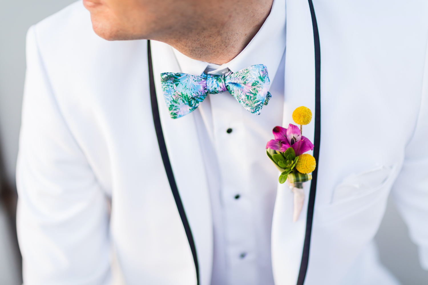 groom wearing blue green tropical bow tie with white tuxedo